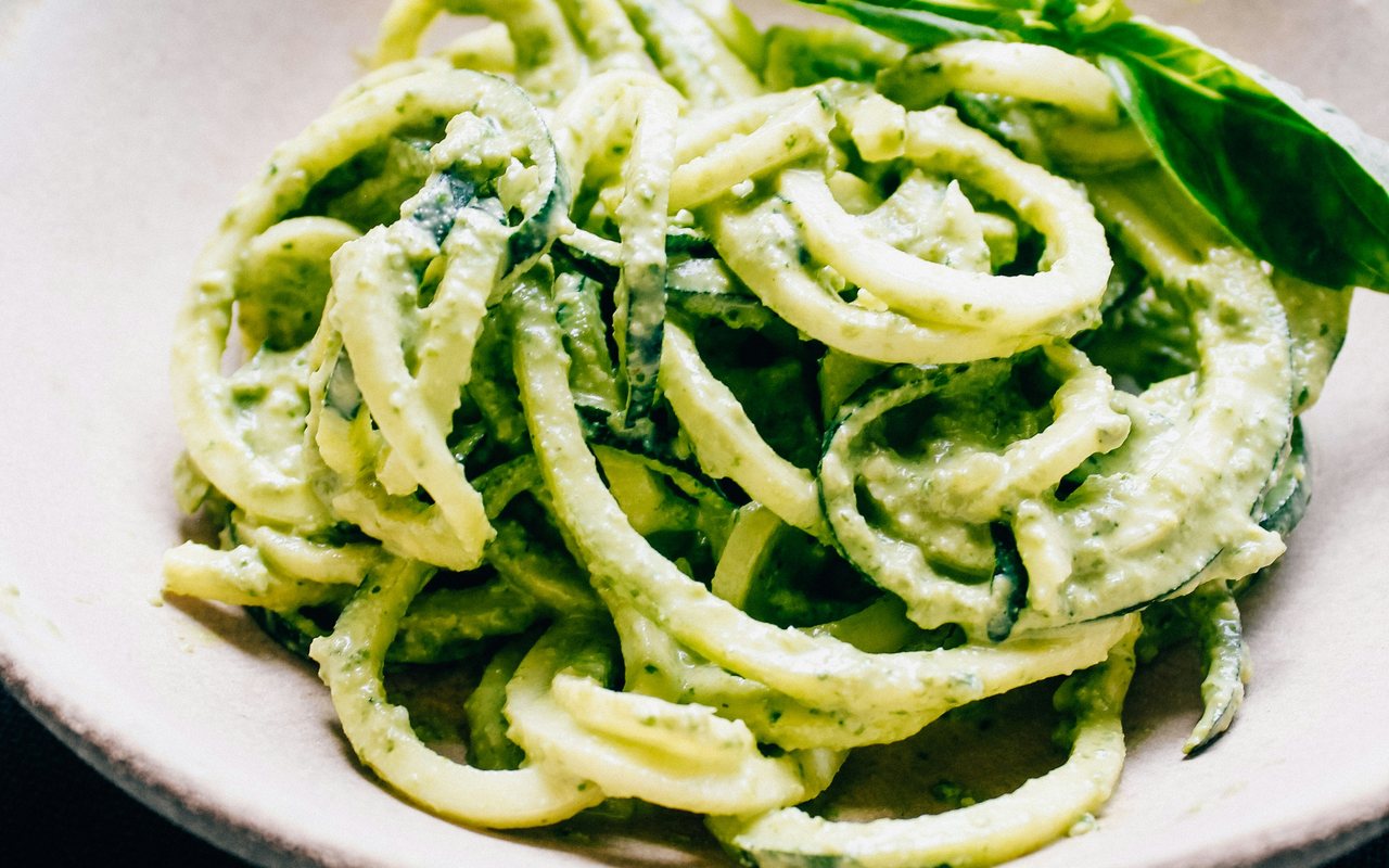 Zucchini noodles coated in green pesto and topped with basil in a white bowl.