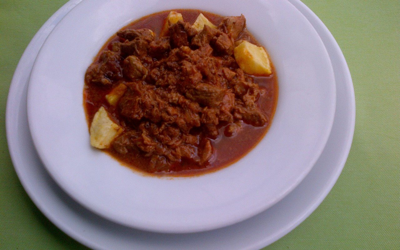 Chunks of braised beef and potatoes in tomato-red sauce on a white plate
