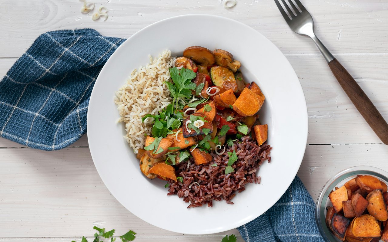 A bowl of roasted sweet potatoes, two types of rice, sauteed mushrooms and peppers, scallions, and cilantro.