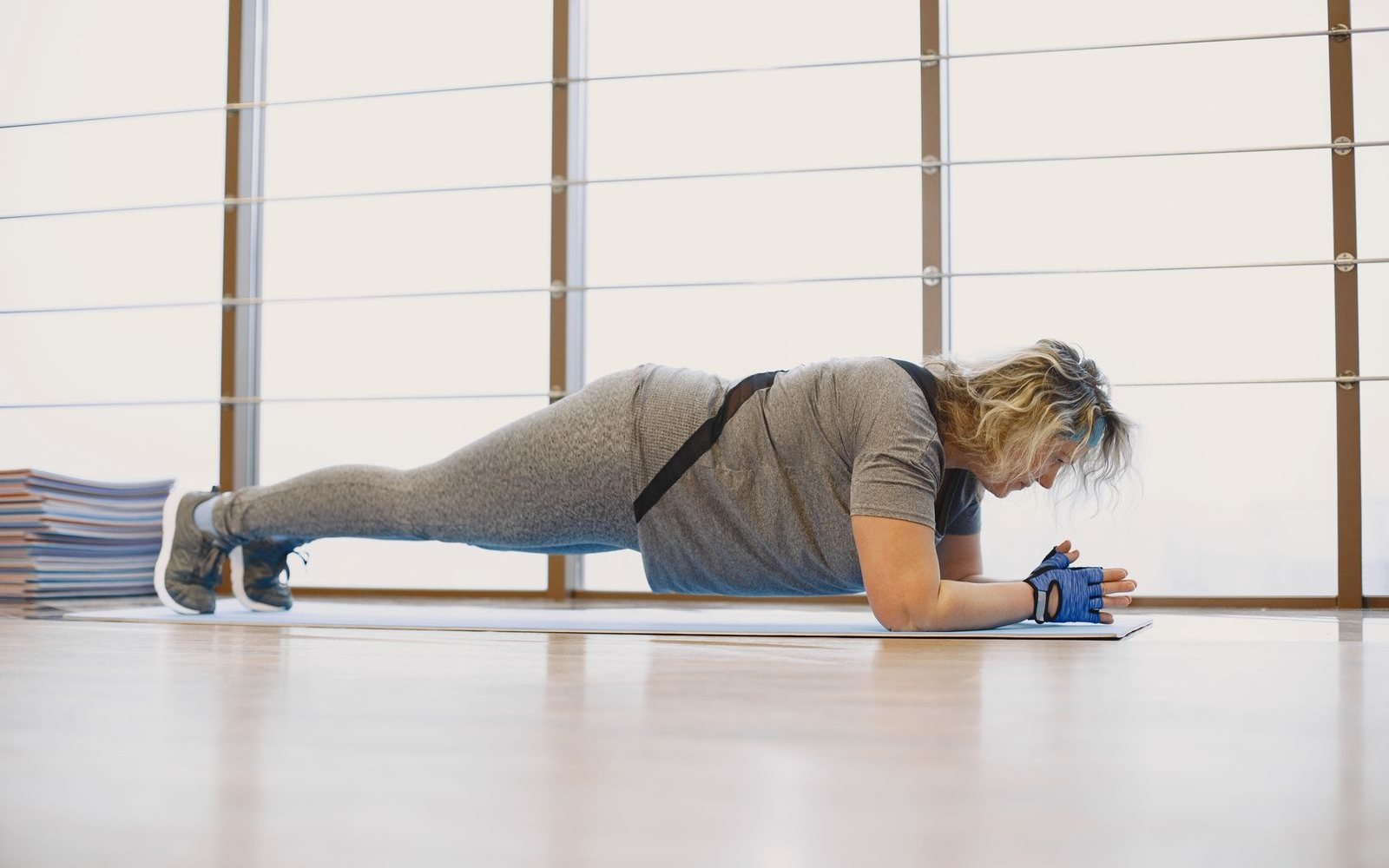 Woman holding a forearm plank on a mat in a bright studio.