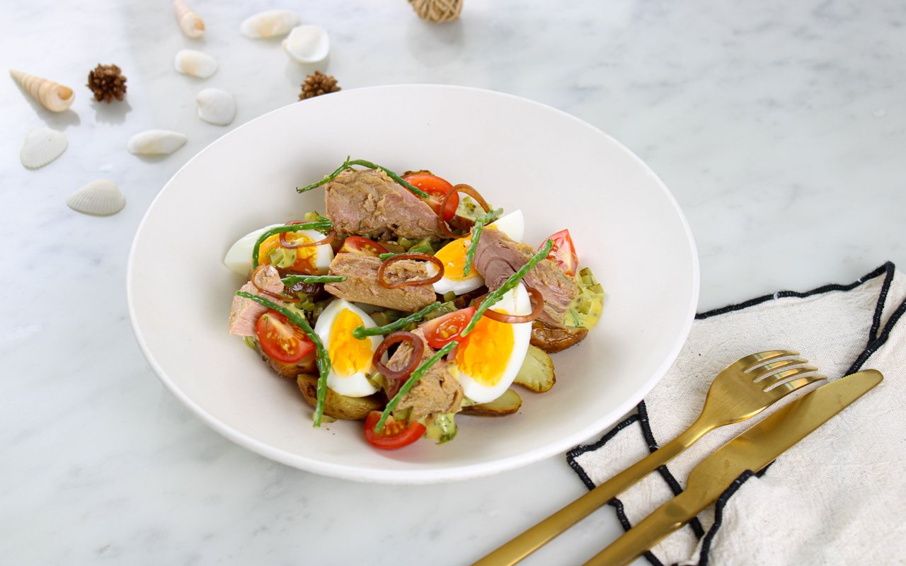 Bowl of tuna salad with halved egg, avocado, spinach, and strawberries