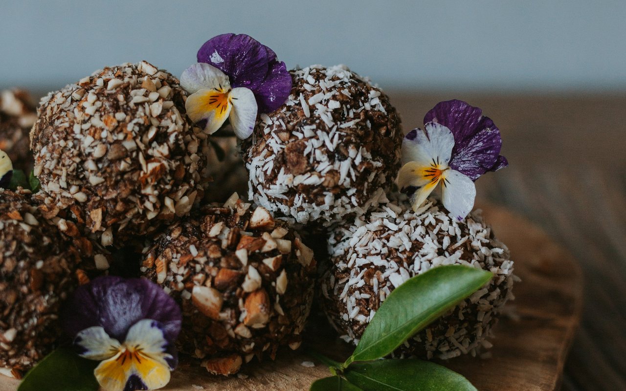 Coconut- and nut-coated oat energy bites decorated with edible flowers on a wooden plate.