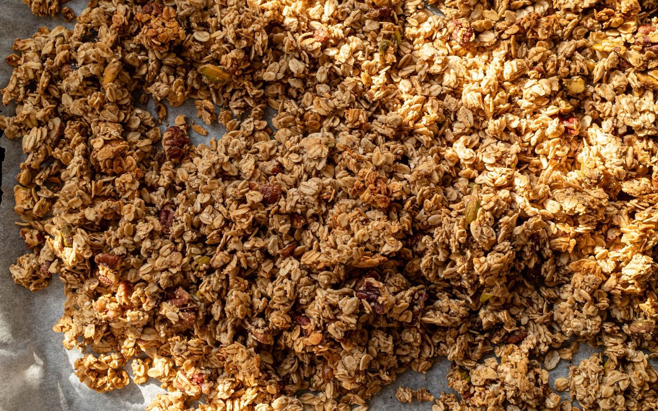Golden oat granola with mixed nuts and pumpkin seeds spread on a parchment-lined pan