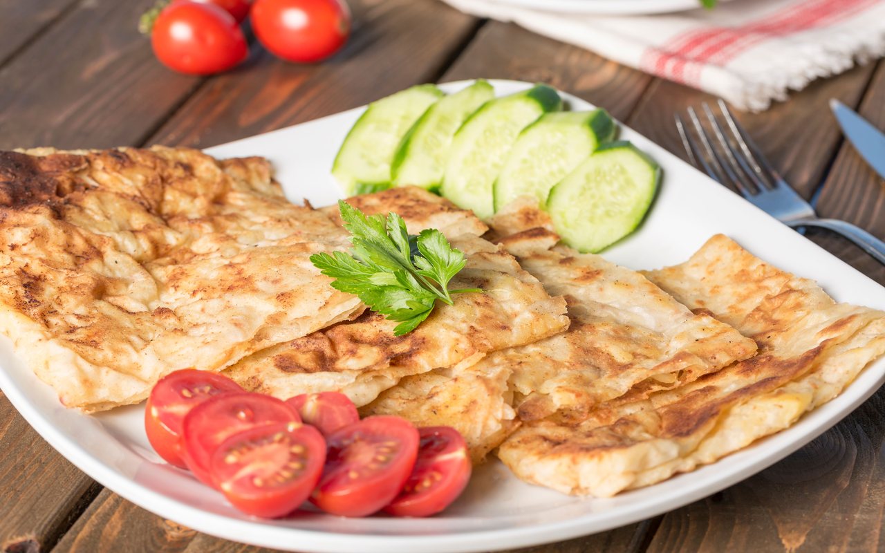 Golden folded Turkish gözleme served with sliced tomatoes, cucumber, and parsley