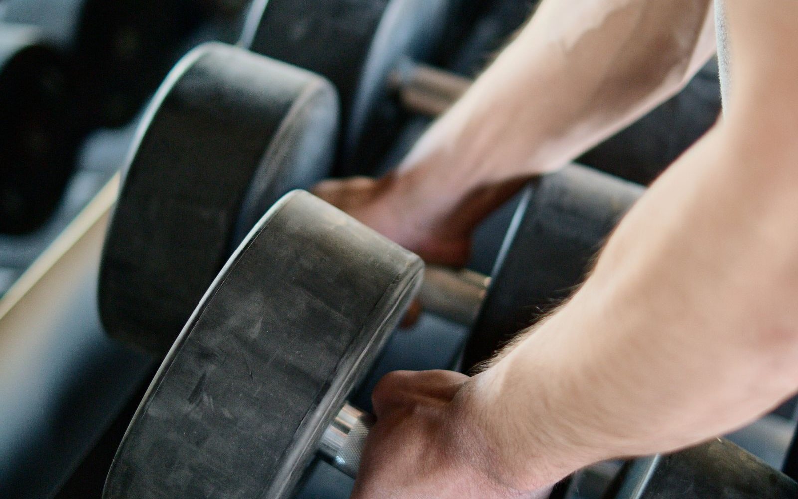 Hands guide a pair of dumbbells at a storage rack.