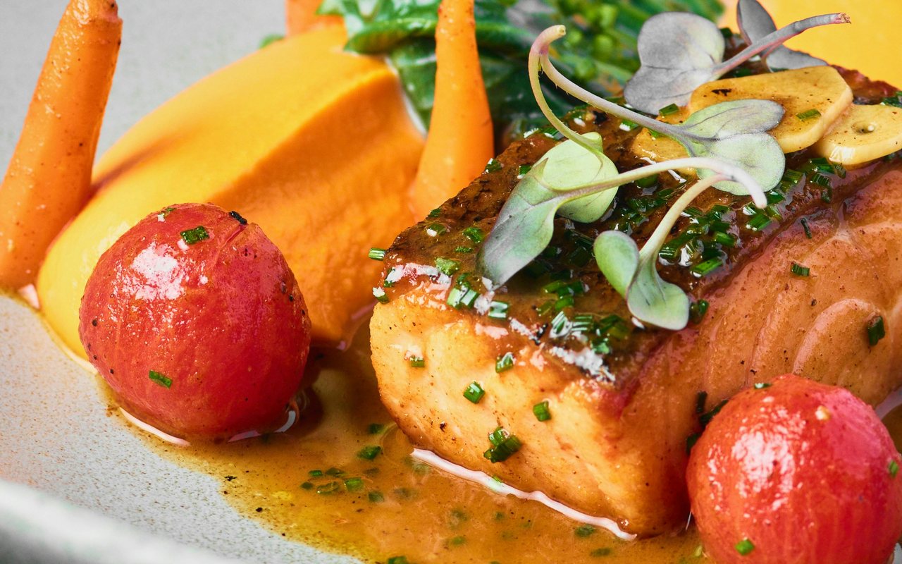 Cooked salmon fillet with potatoes, carrots, asparagus, and leafy greens.