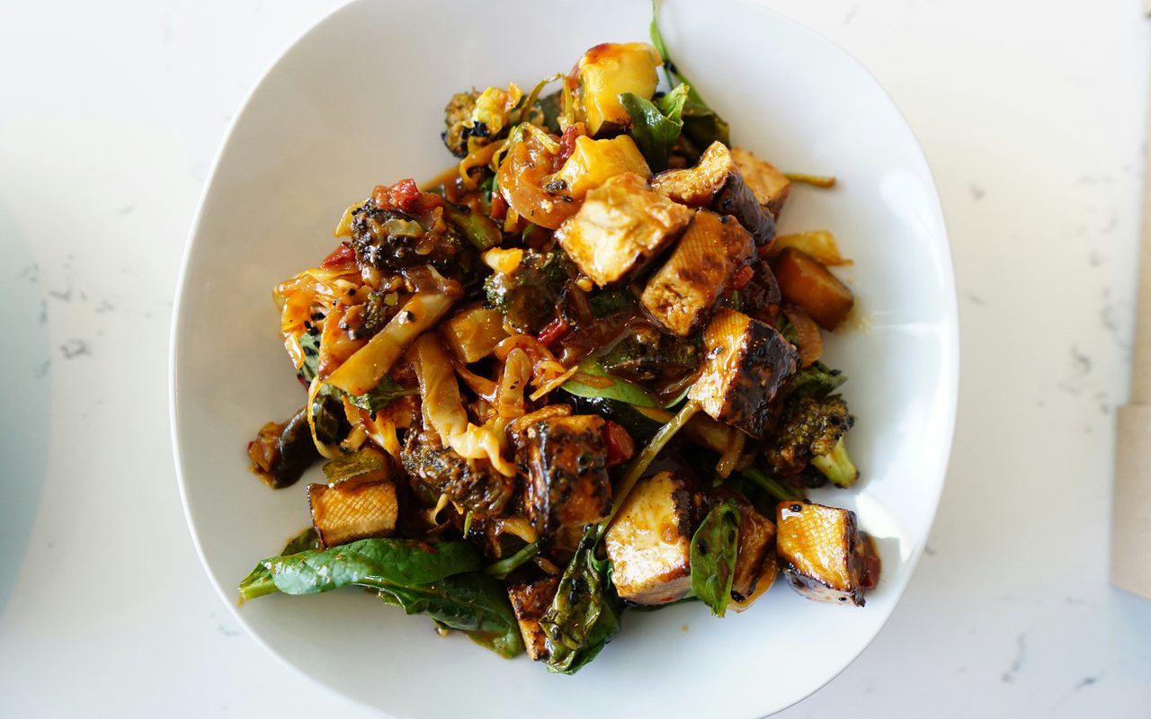 Browned tofu with broccoli, leafy greens, cabbage, baby corn, and other vegetables in sauce.