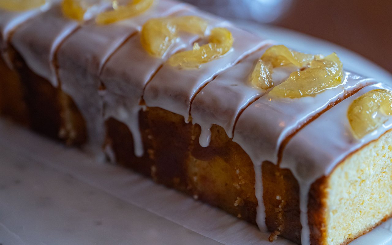 Sliced lemon loaf cake coated with white glaze and topped with curled lemon peel