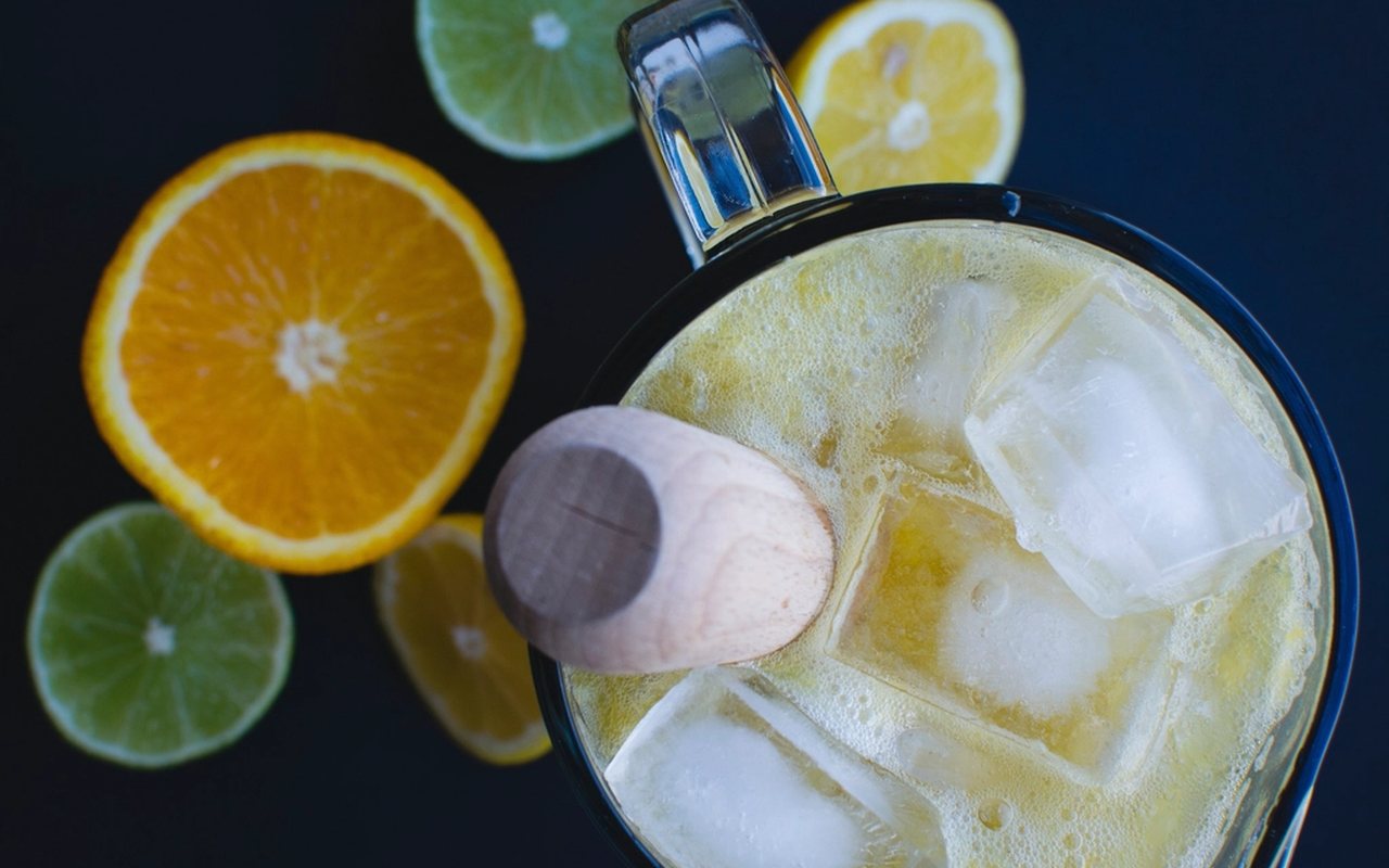 Cold pale-yellow lemonade in a glass pitcher with citrus slices