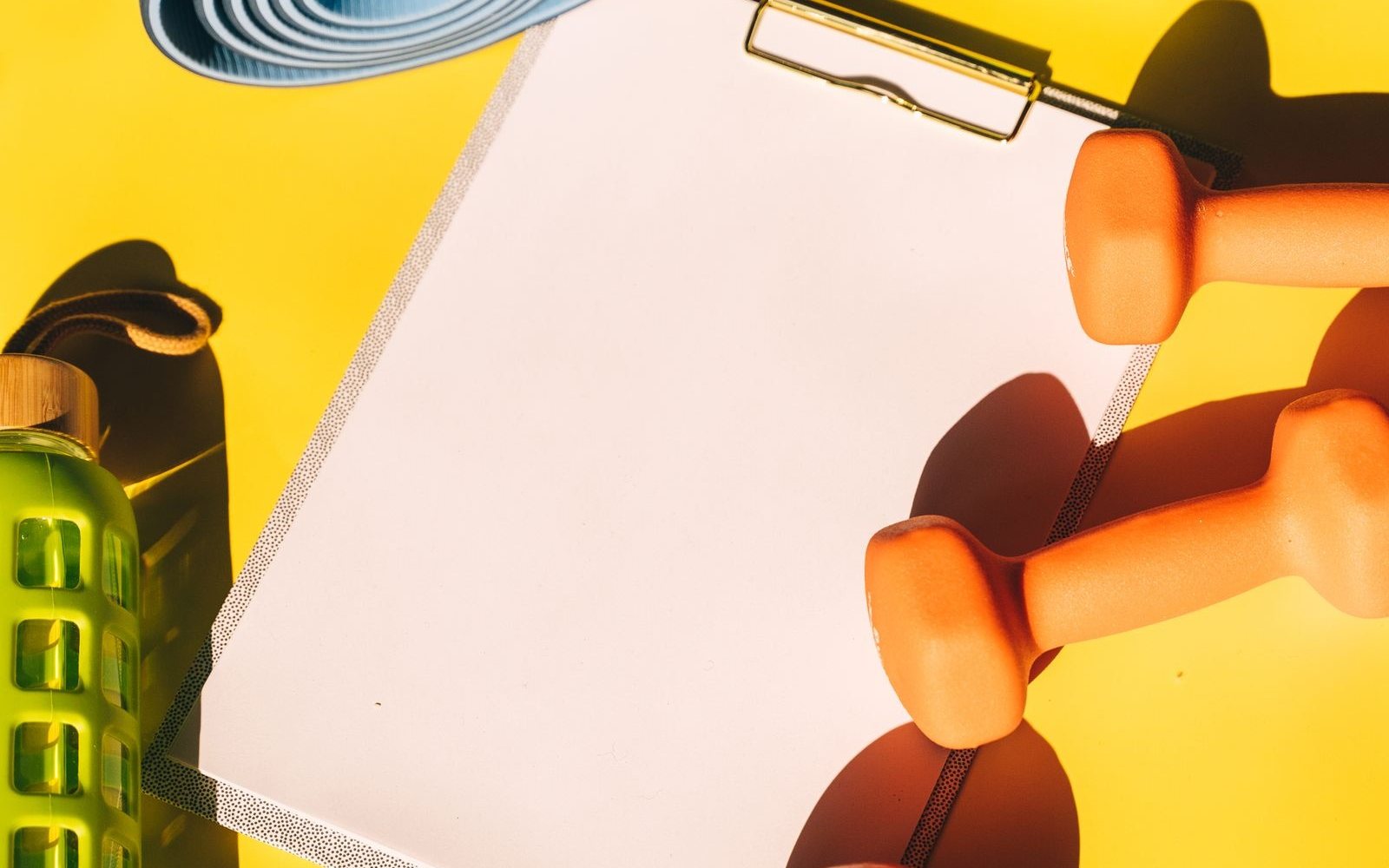 Blank clipboard surrounded by dumbbells, a water bottle, and an exercise mat.