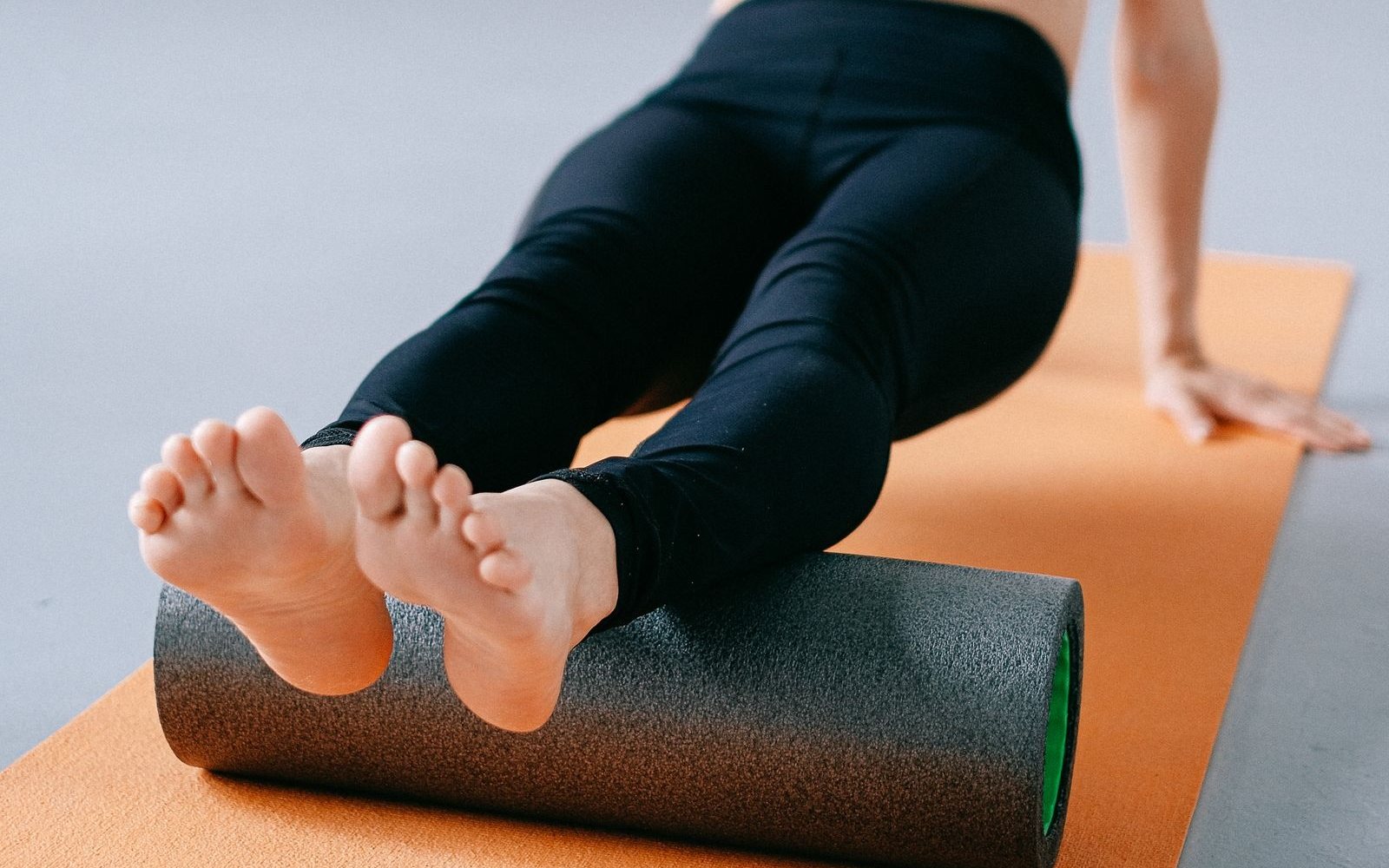 Person resting both calves on a foam roller on an exercise mat.