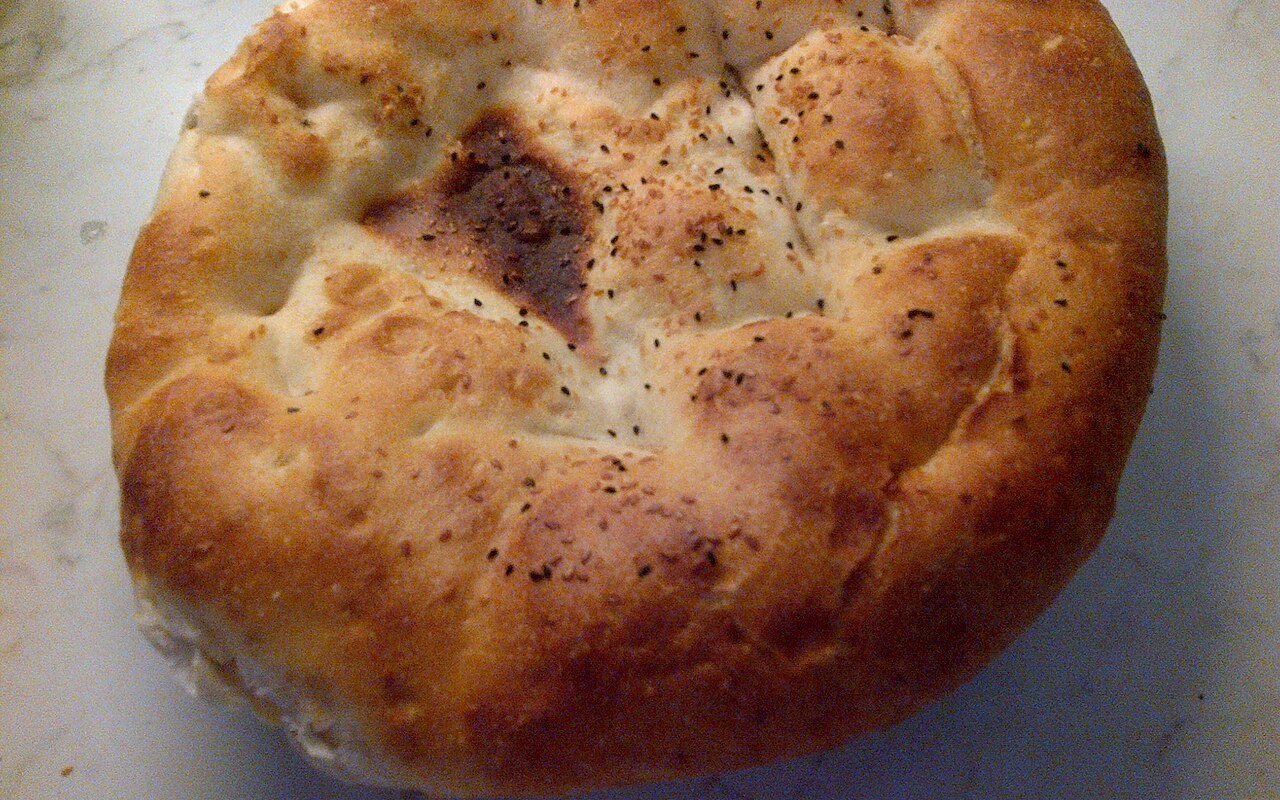 Two round dimpled Ramazan pidesi breads topped with sesame and nigella seeds