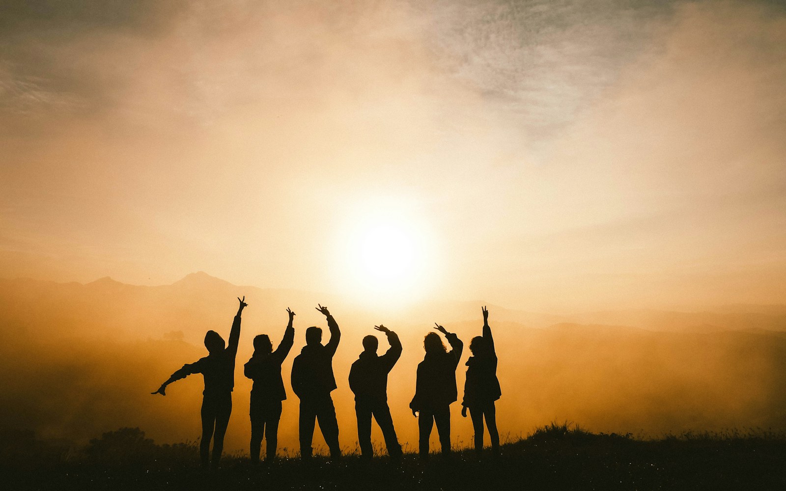 Silhouettes of six friends together on a ridge at sunrise