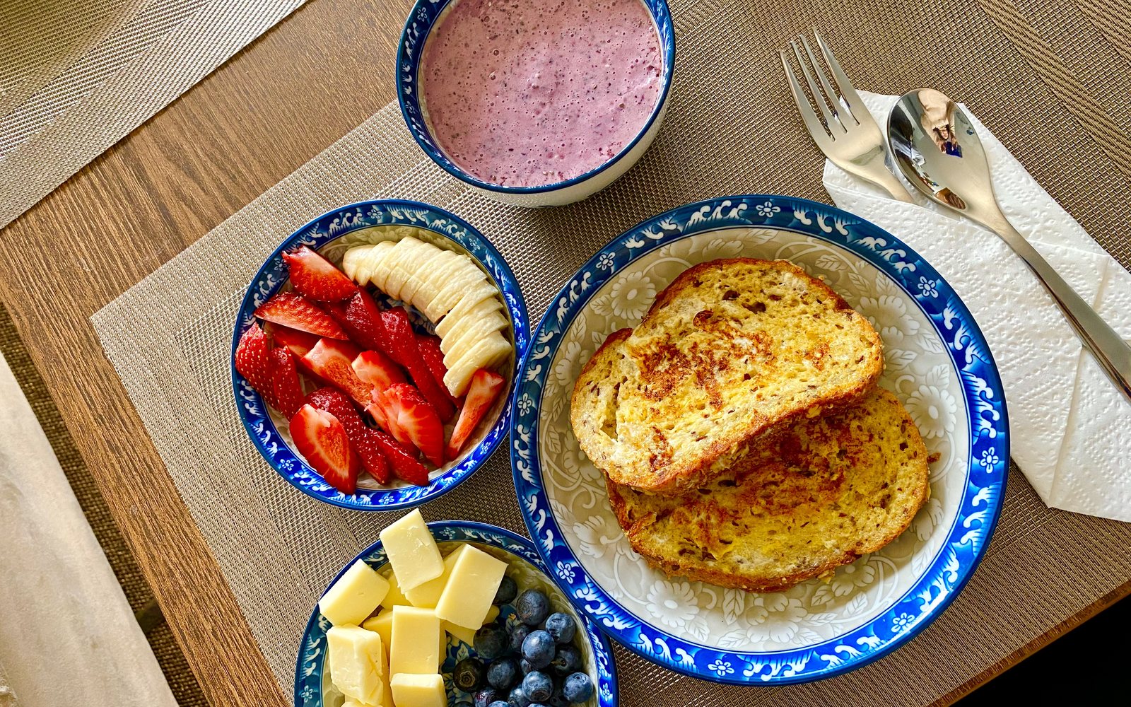 Overhead breakfast spread with toast, fruit, cheese, berries, and a smoothie.