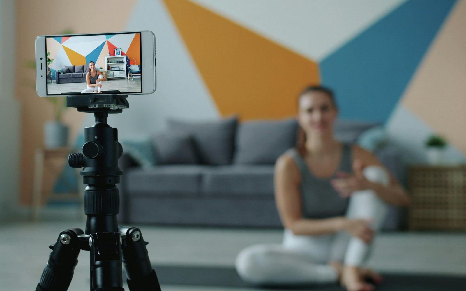 Smartphone mounted on a tripod records an adult exercising on a mat.