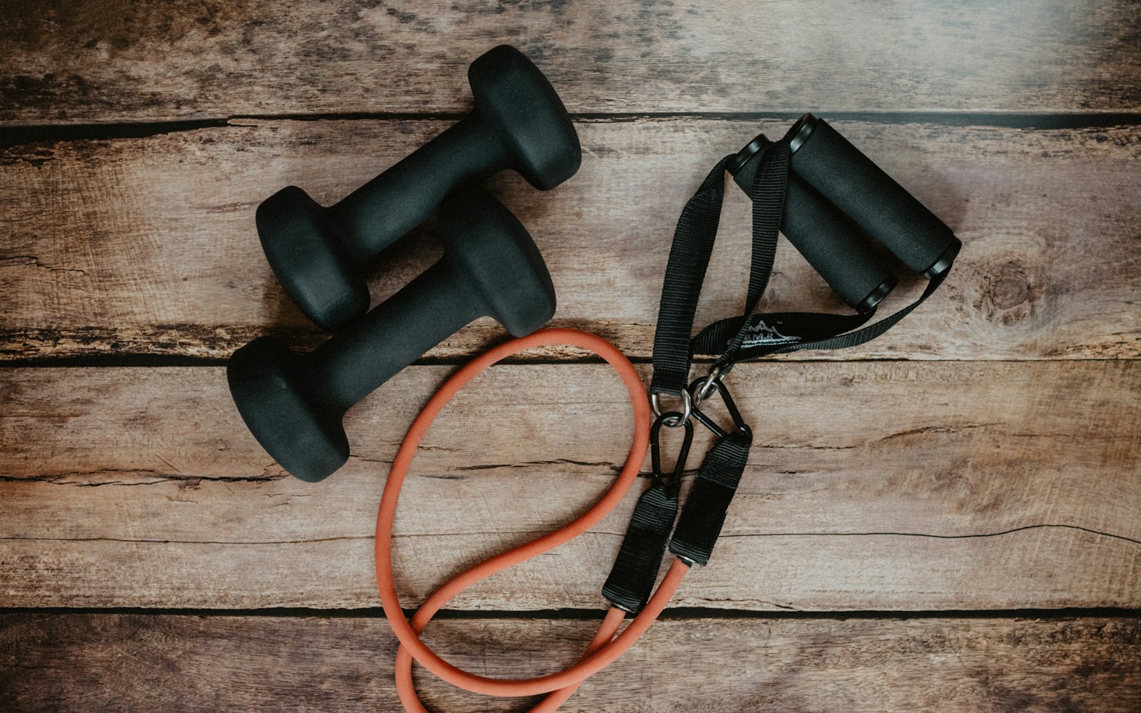 Dumbbells, resistance tubing, and push-up handles arranged on a wooden floor