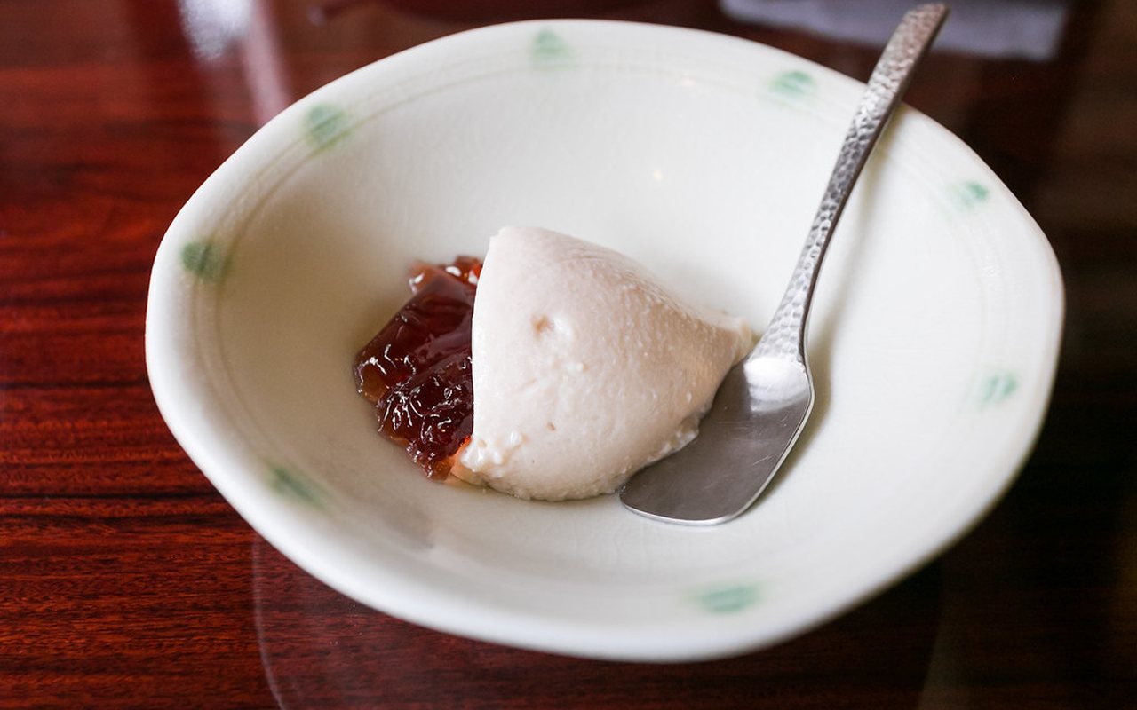 A molded scoop of pale milk pudding served with red fruit preserve in a shallow bowl