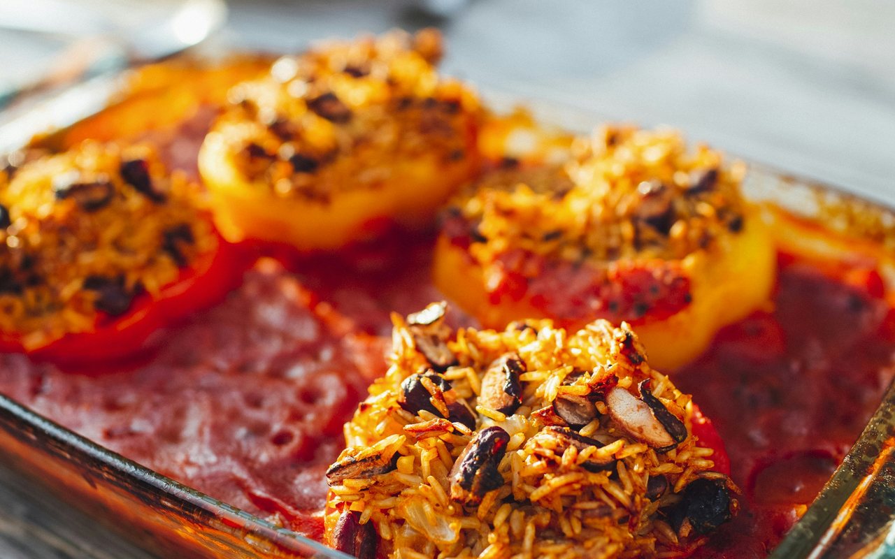 Rice-and-black-bean stuffed red and yellow peppers baking in tomato sauce.