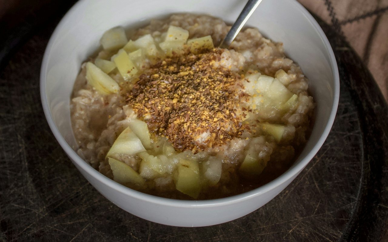 Apple-topped oatmeal sprinkled with brown spice in a white bowl.