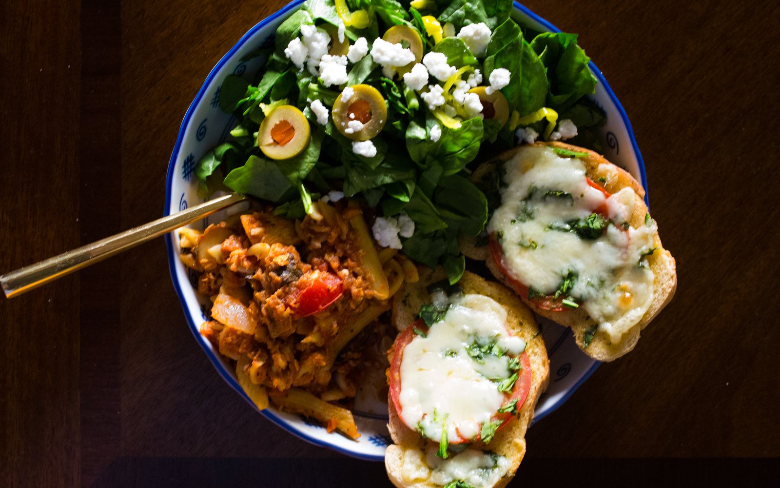 Plate with leafy salad, a mixed pasta dish, and tomato-cheese toast.
