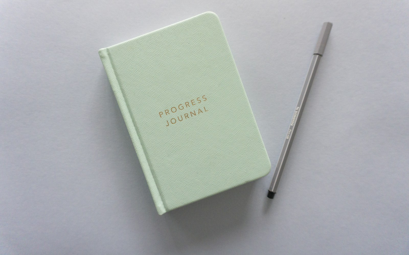 Pale green progress journal beside a pen