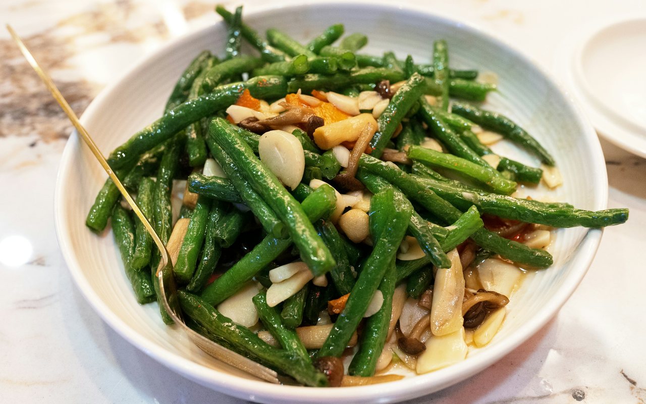 Green beans tossed with mixed nuts in a white bowl.