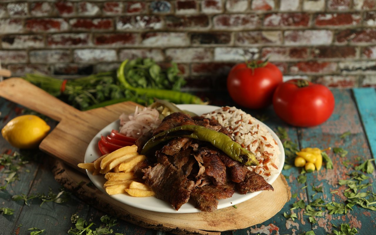 Browned döner slices with rice, fries, tomatoes, onion, and a roasted green pepper