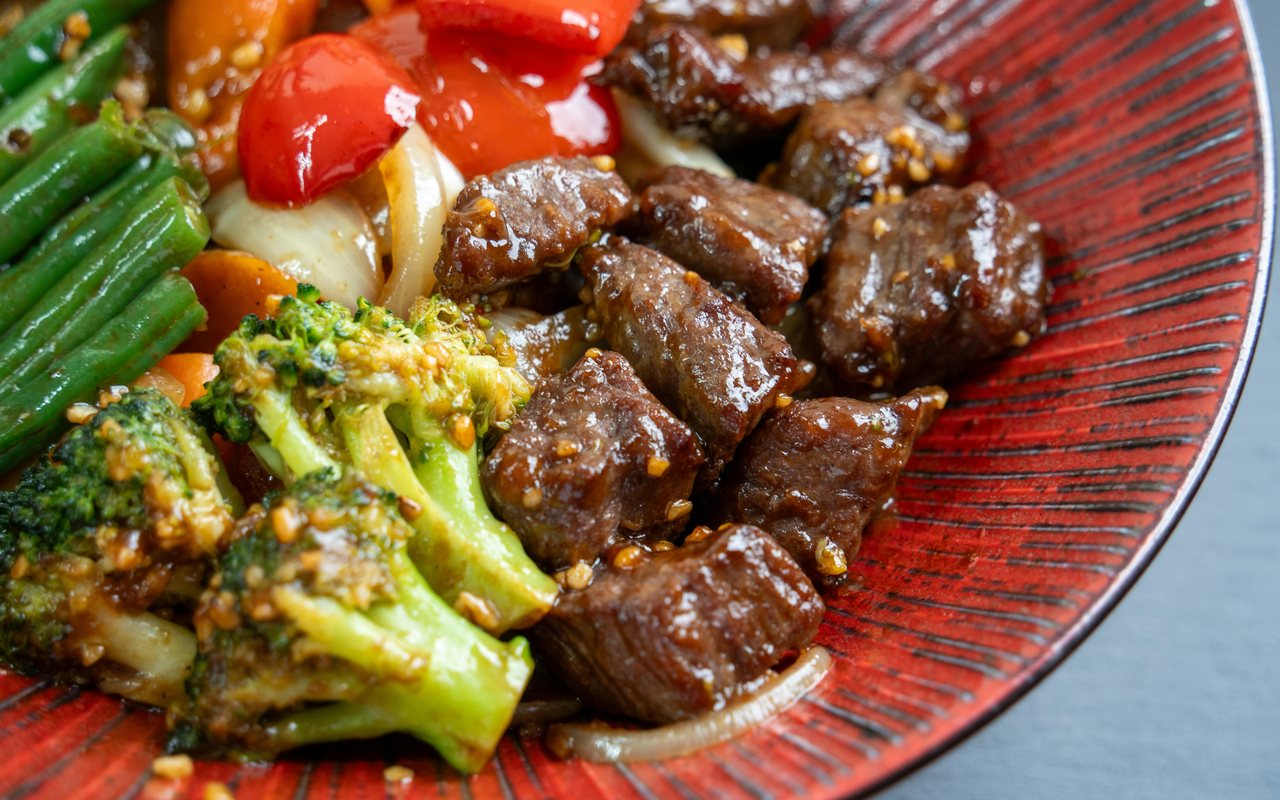 Beef and broccoli stir-fry with green beans, carrots, onions, and red peppers on a red plate.