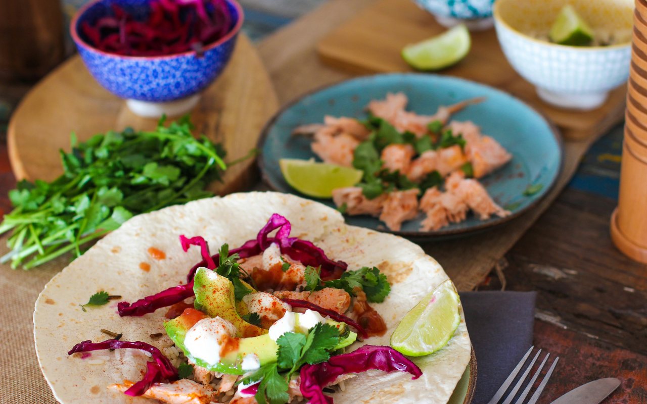 Tortilla wraps filled with flaked cooked salmon, avocado, cabbage, rice, cilantro, and creamy sauce.