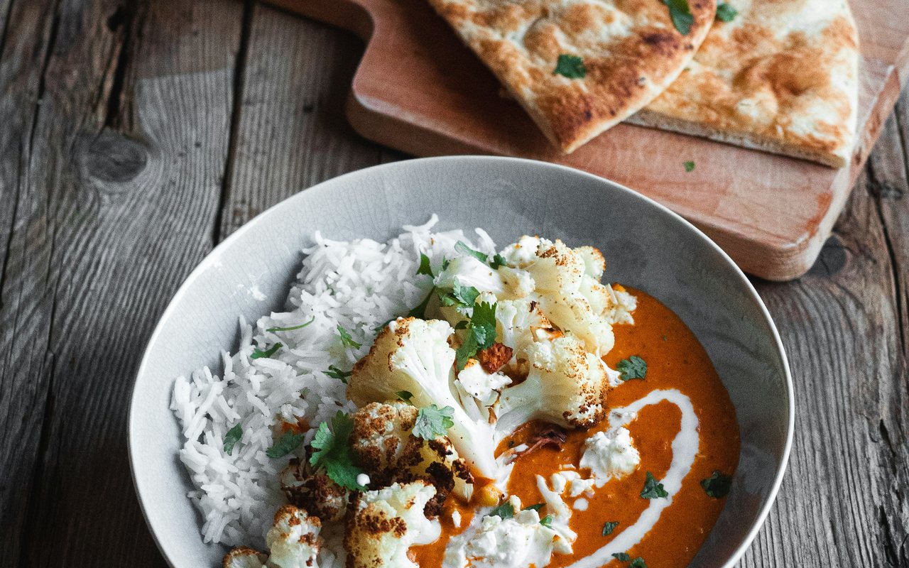 Roasted cauliflower curry with white rice, cilantro, and a yogurt drizzle in a gray bowl.
