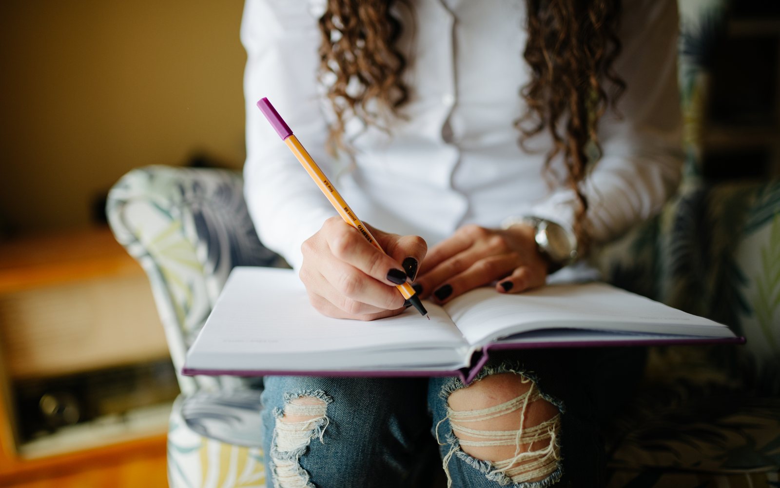 Close-up of an adult writing in an open notebook at a desk.