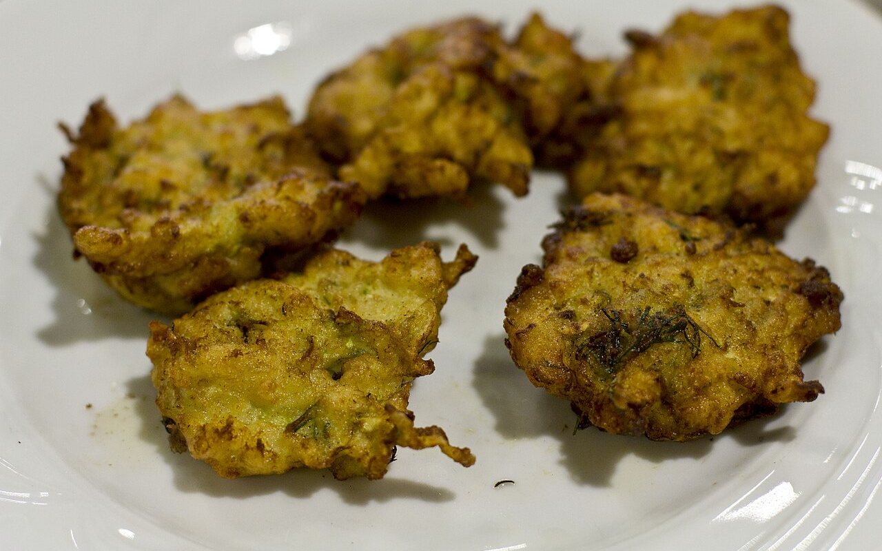 Golden zucchini fritters with visible carrot, scallion, and dill on a plate