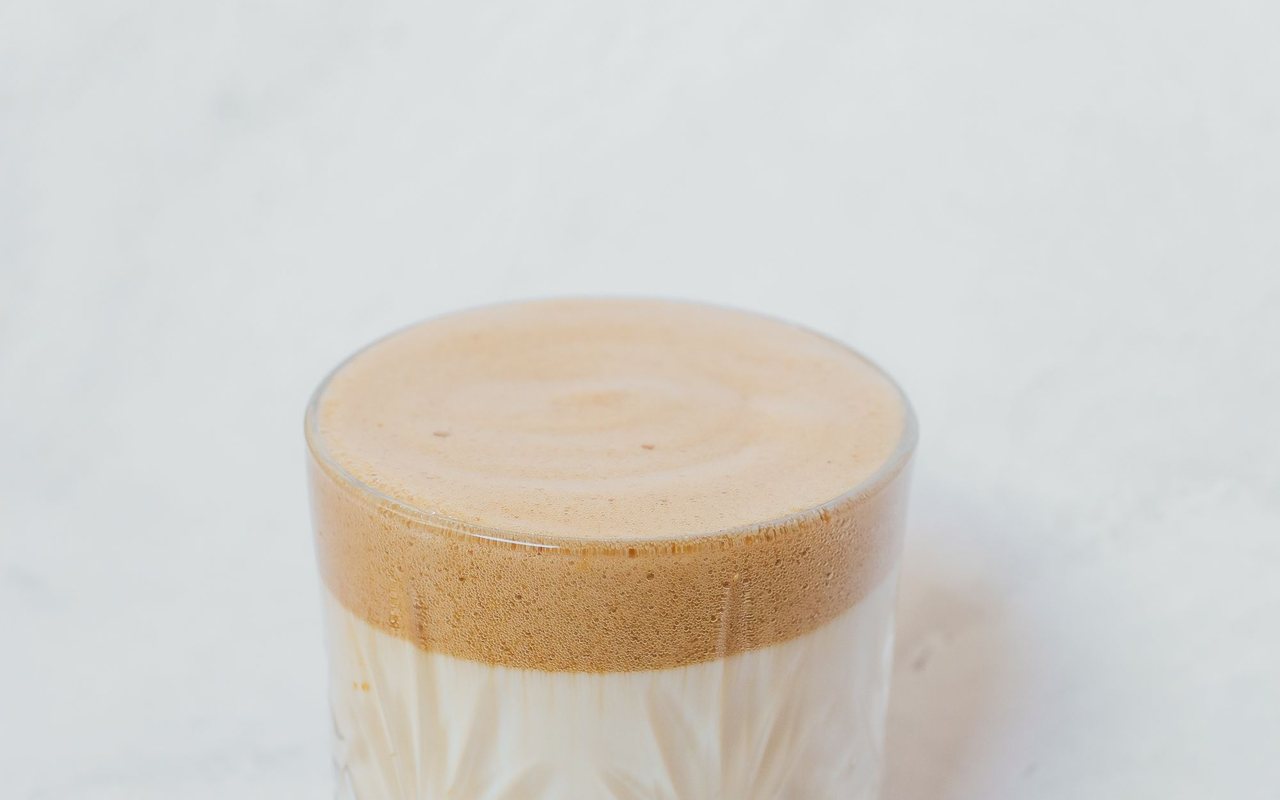 Two glasses of iced milk topped with thick whipped dalgona coffee foam