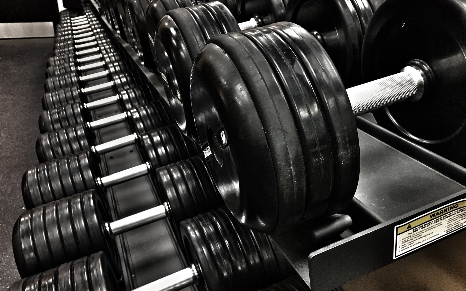 Rows of black dumbbells arranged on a gym rack.