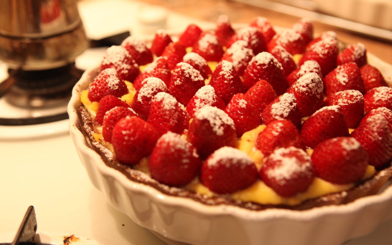 Round tart filled with pale cream and arranged sliced strawberries