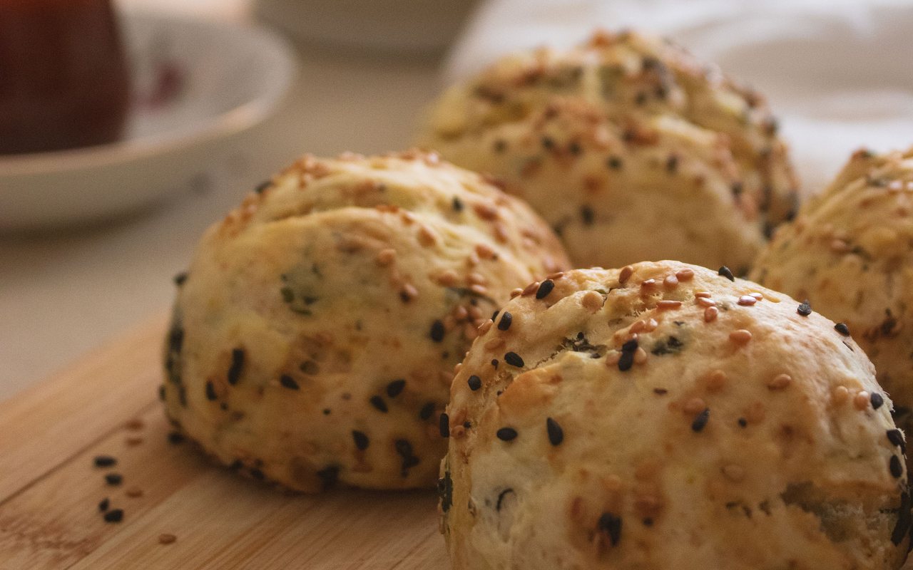 Round golden savory buns topped with sesame and nigella seeds on a wooden board
