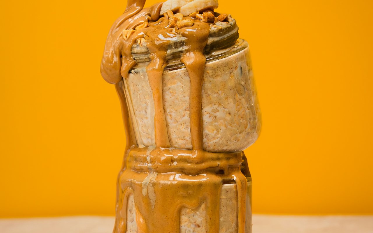 Stacked jars of oats topped with banana slices, chopped nuts, and thick peanut butter drizzle.