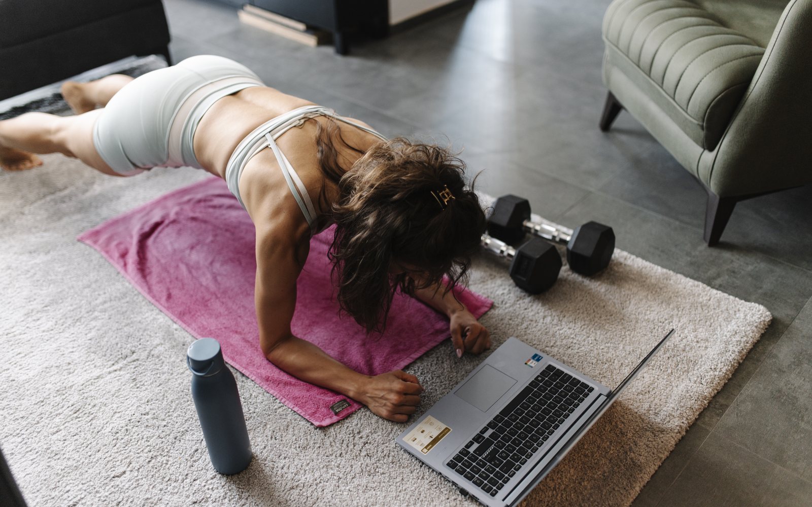 Woman holds a forearm plank at home while watching an open laptop.