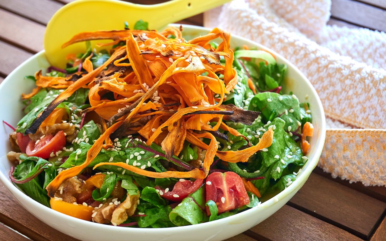 Leafy green salad with roasted orange carrot ribbons, tomatoes, walnuts, and sesame seeds