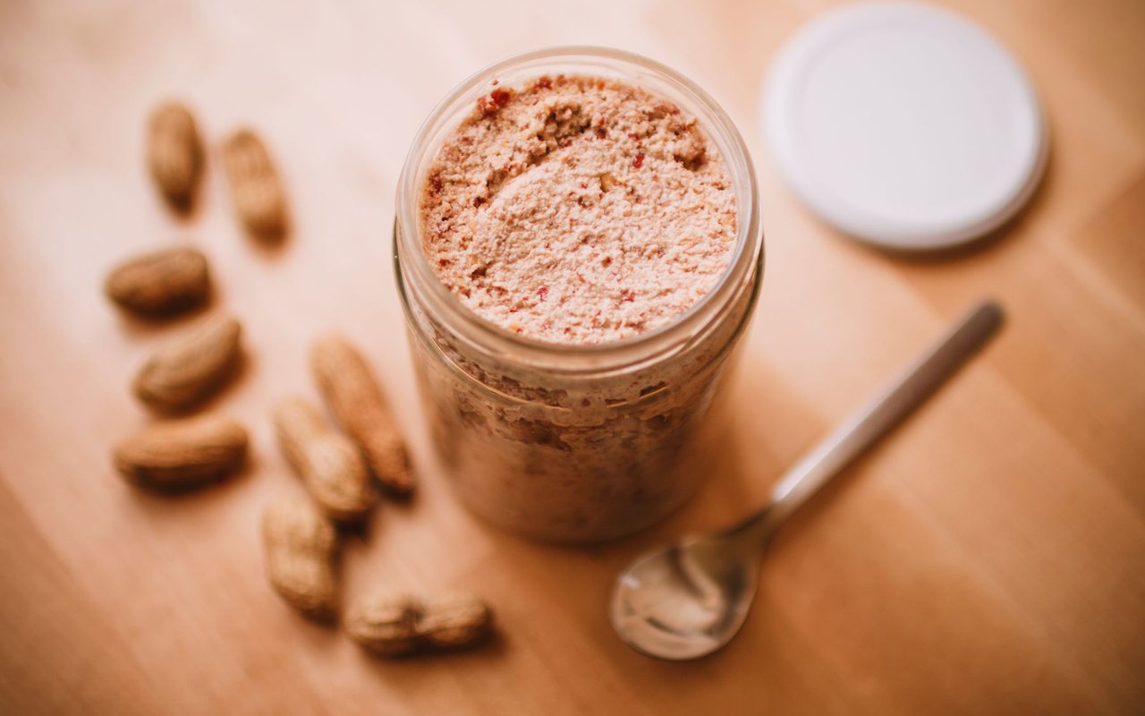 Creamy homemade peanut butter in a glass jar beside roasted peanuts