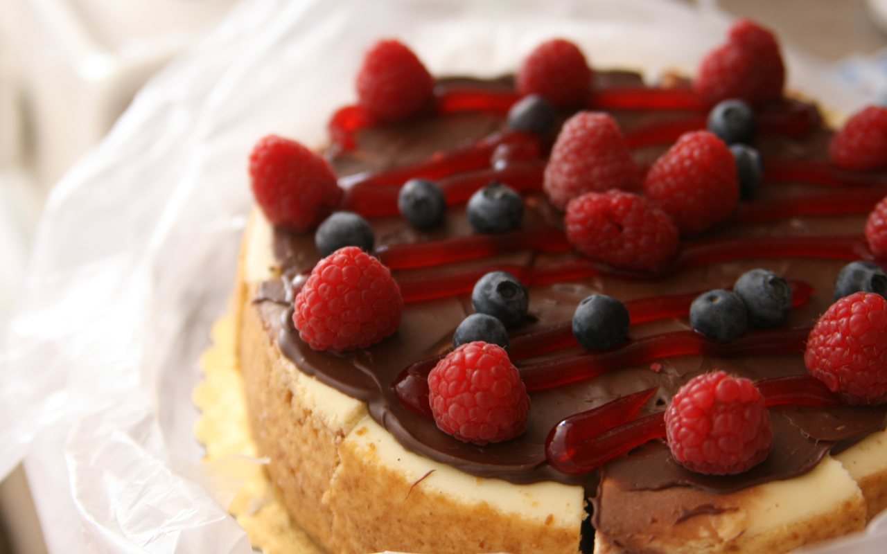 Whole cheesecake topped with chocolate, red fruit glaze, raspberries, and blueberries