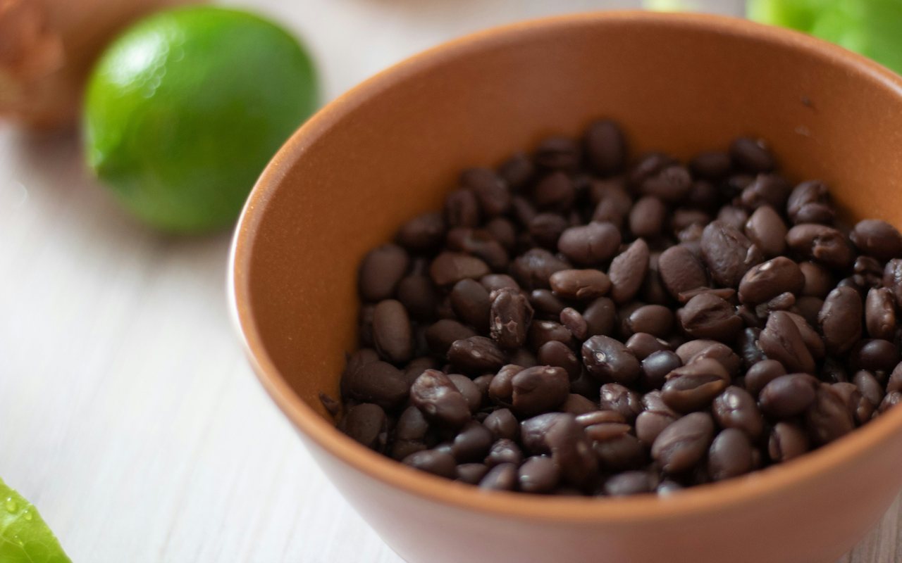 Bowl of cooked black beans beside halved limes on a dark surface.