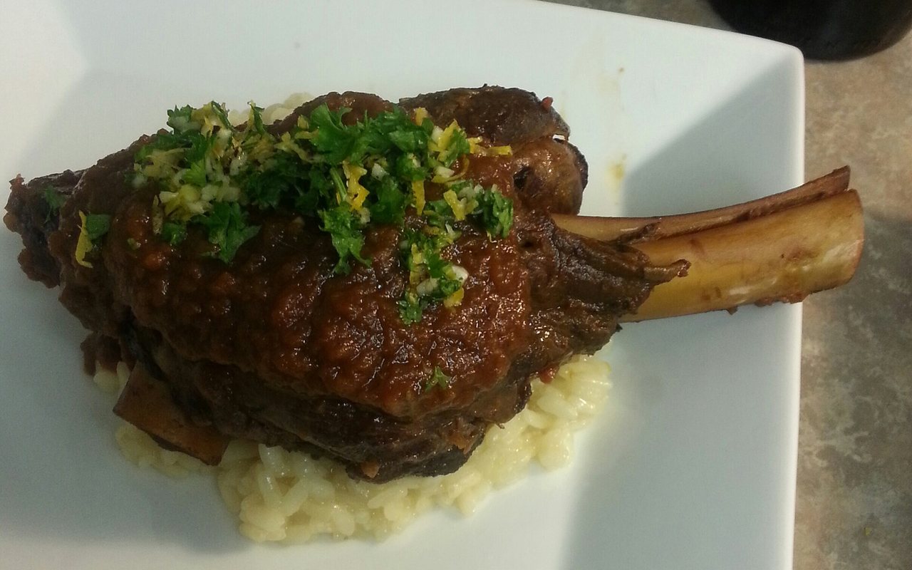 Braised lamb shanks with potatoes, carrots, shallots, and herbs in a roasting dish