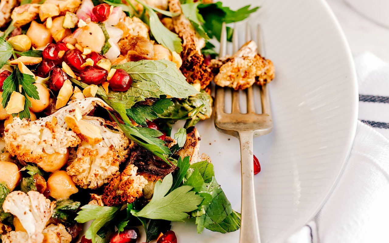 Roasted cauliflower and chickpeas with parsley, mint, pomegranate seeds, and chopped nuts on a white plate.