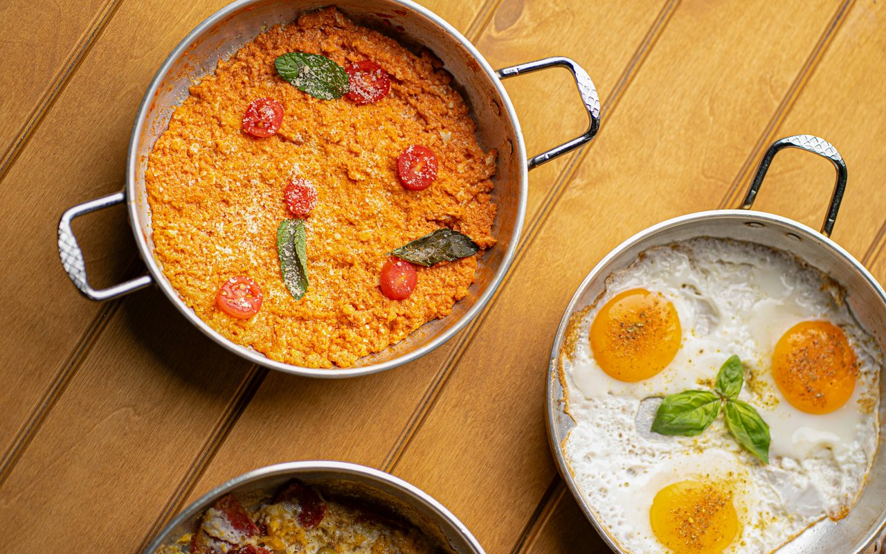 A skillet of tomato scrambled eggs beside a pan of fried eggs on a wooden table
