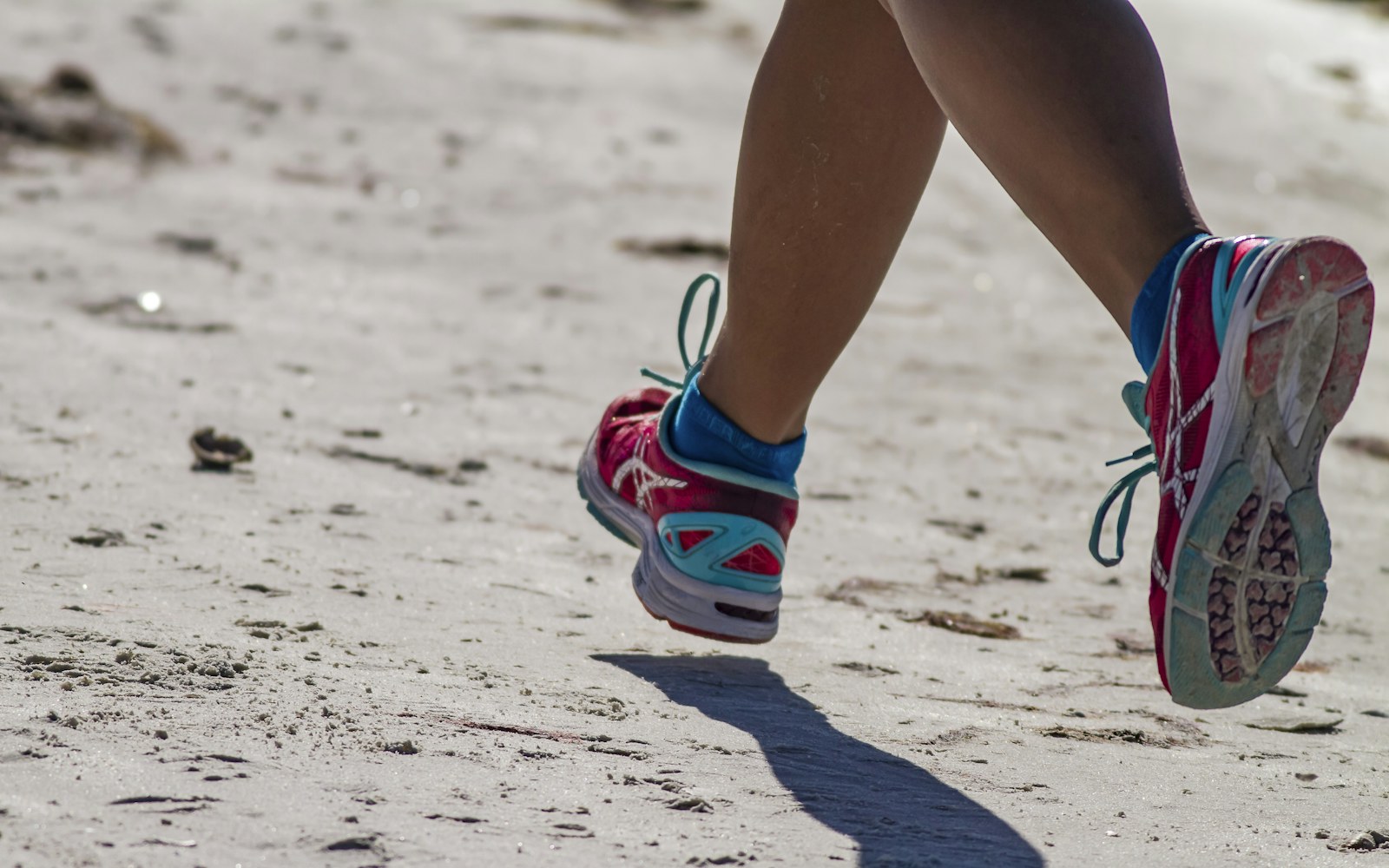 Close-up of a person jogging across firm sand