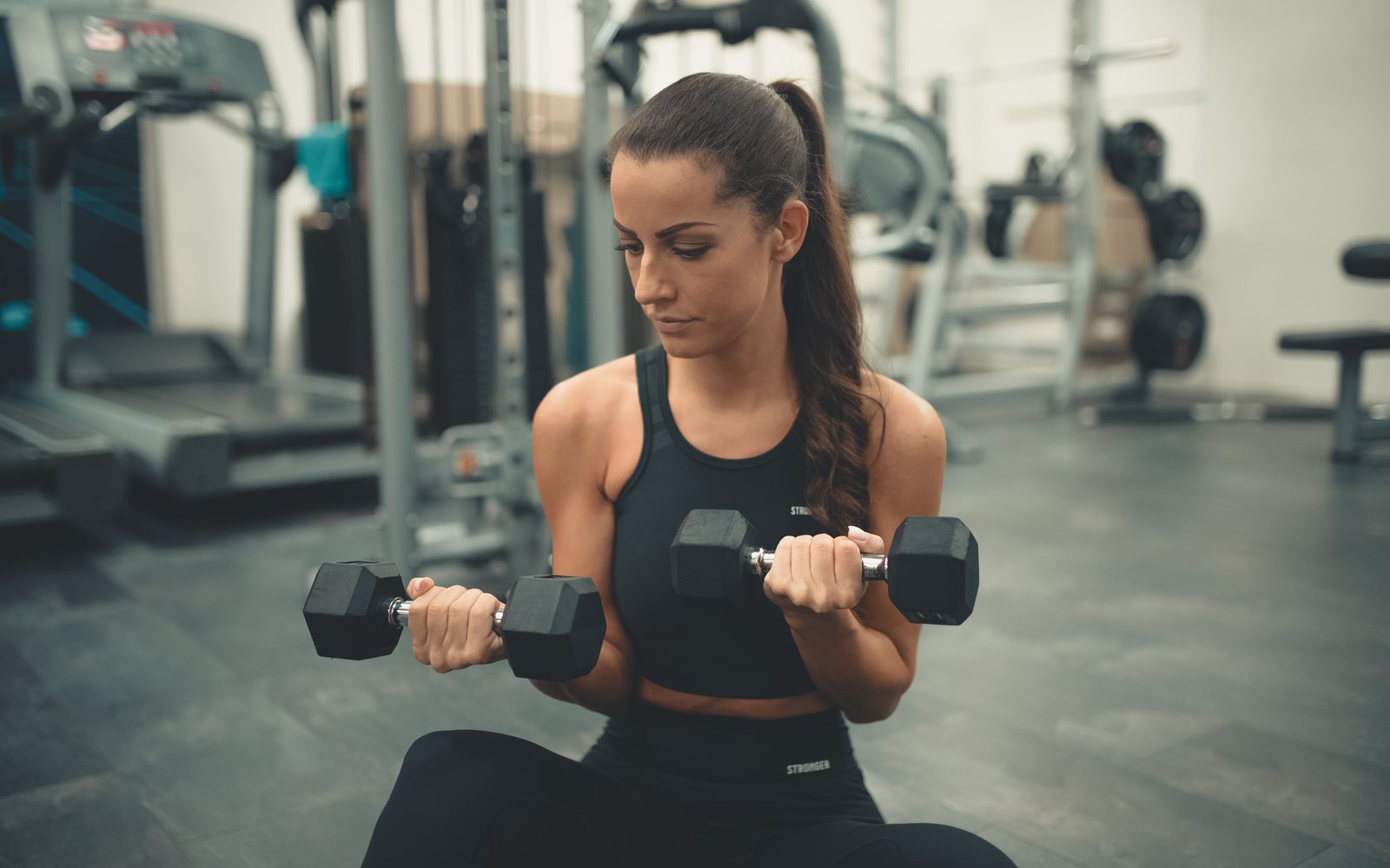 Woman seated in a gym performing dumbbell curls.