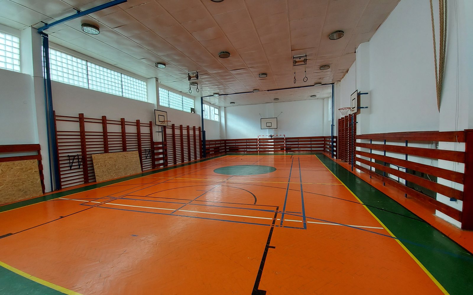 Empty indoor gymnasium with a polished court, basketball hoops, and orange walls.