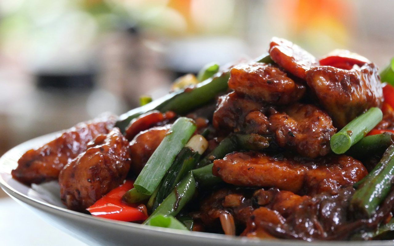 Glossy sauced chicken with red and green peppers and scallions on a metal platter.