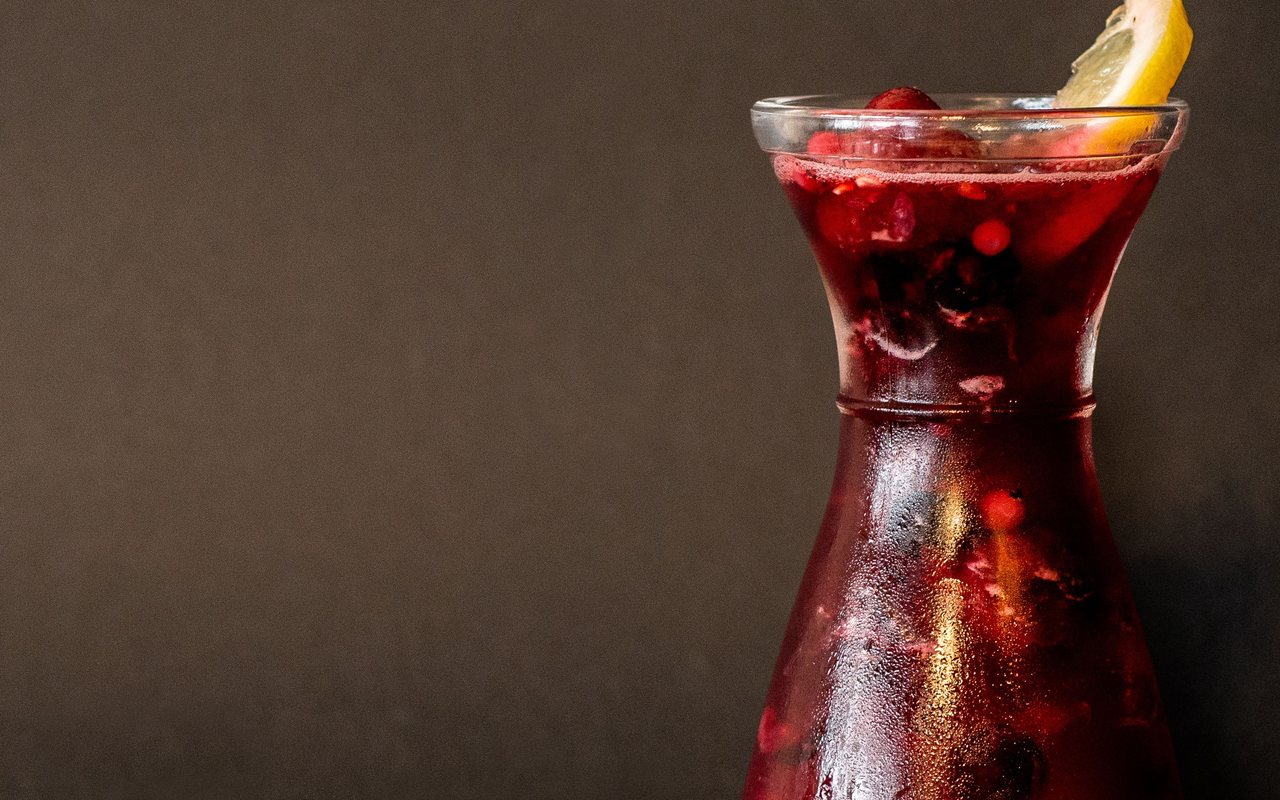 Red berry lemonade in a glass carafe with a lemon wedge